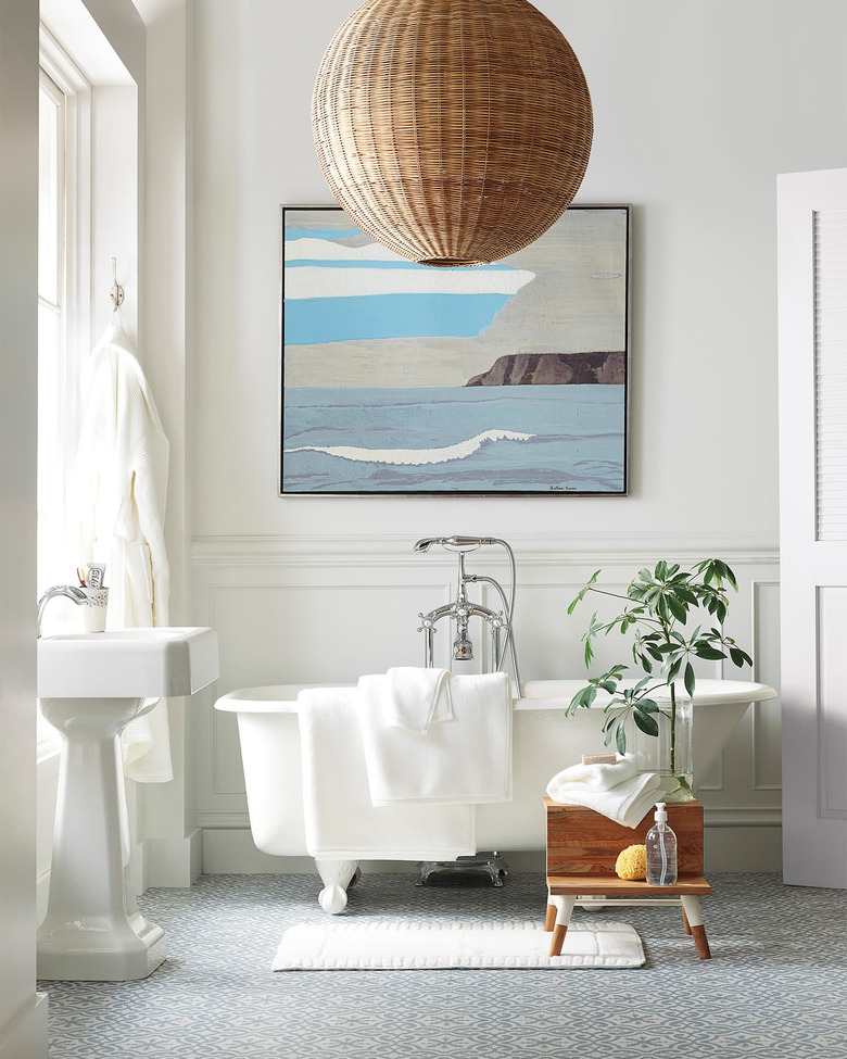 Rattan round coastal bathroom lighting idea in white bathroom alongside freestanding bathtub and coastal artwork