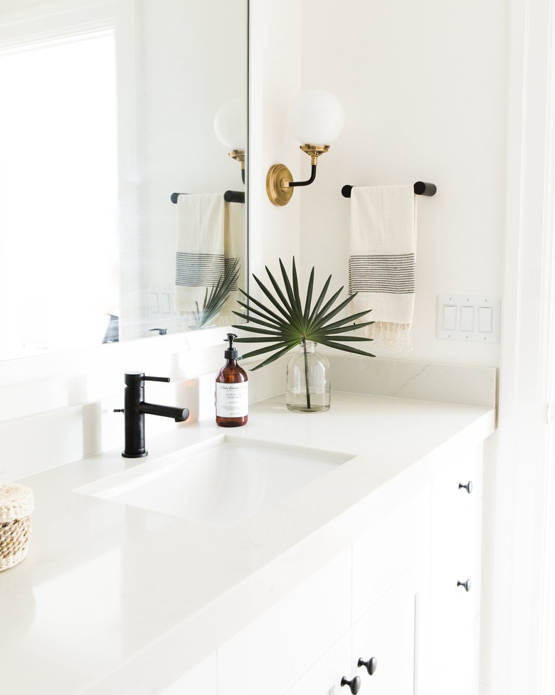 Brass globe-style coastal bathroom lighting idea in all-white bathroom with palm frond