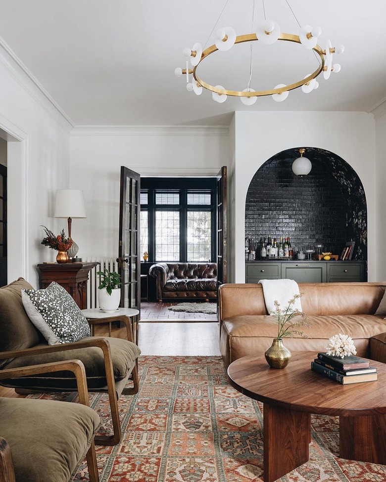 A white-walled living room is anchored by a caramel leather sofa and two olive green velvet side chairs