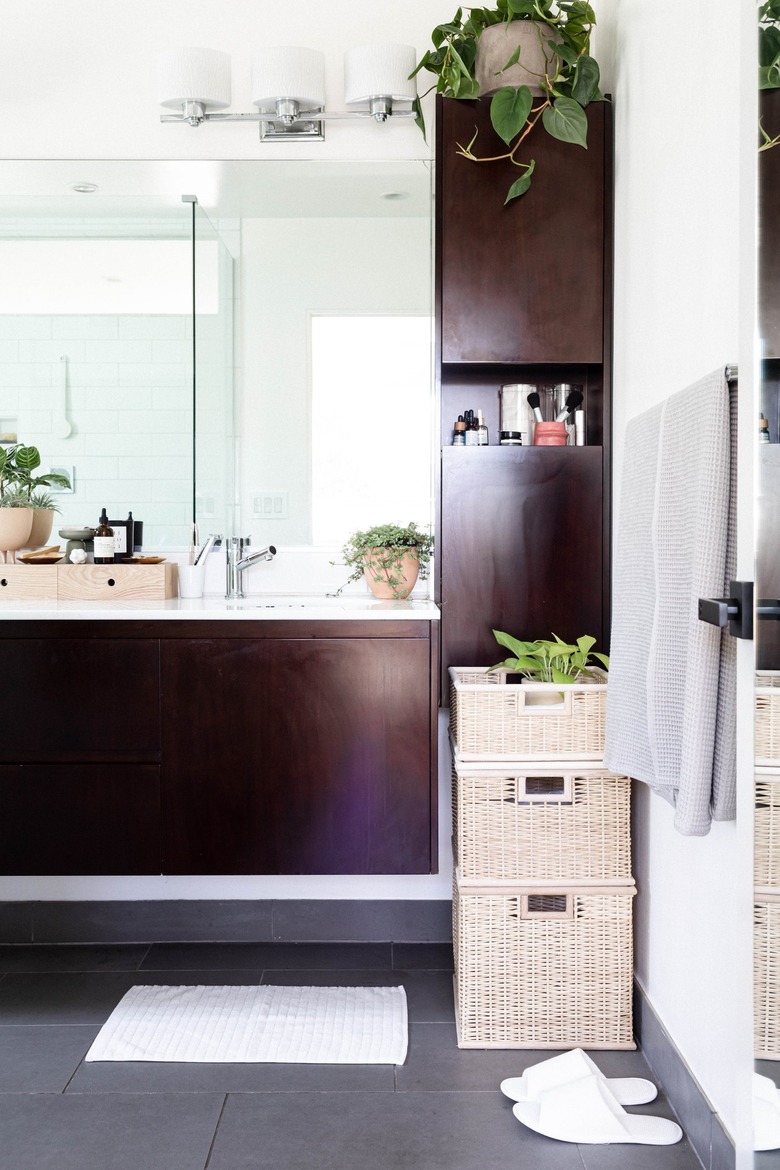 dark wood vanity and gray bathroom floor tile and woven baskets with gray towels