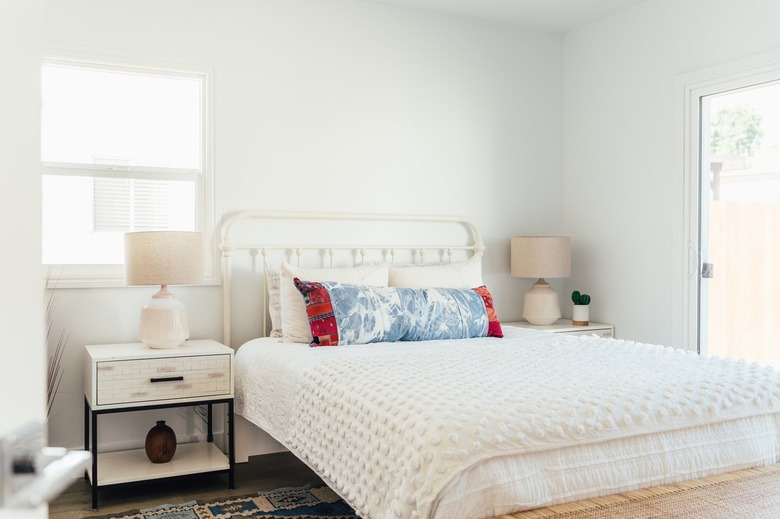 A bedroom with white bedding and blue-red pillows