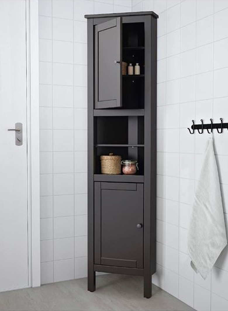 Tall brown corner bathroom cabinet in white-tiled bathroom