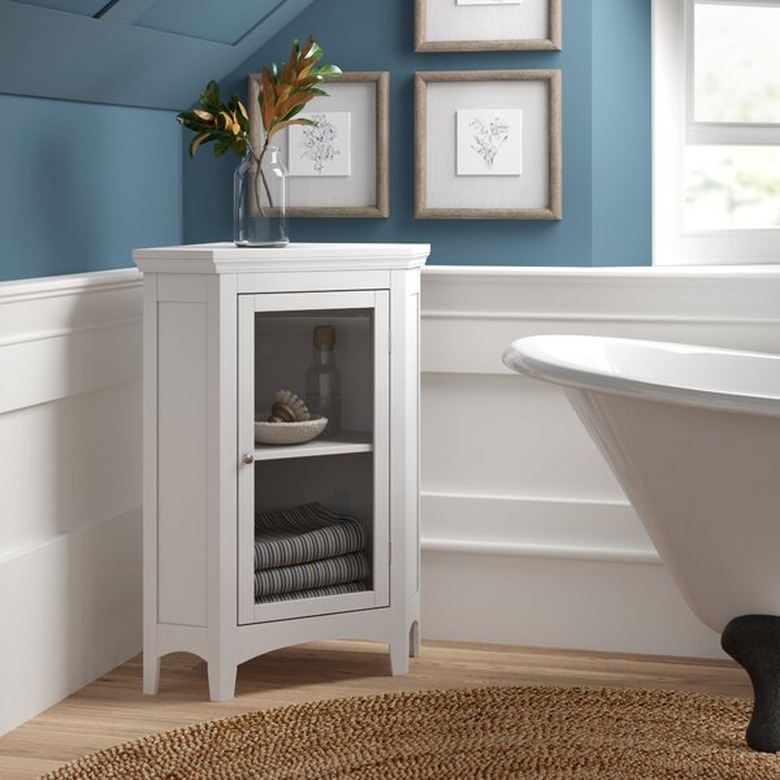 Low white corner bathroom cabinet with clawfoot bathtub and blue–painted walls