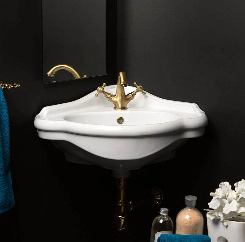 White wall mount corner bathroom sink with brass faucet in black bathroom
