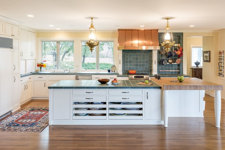 Kitchen with a large island with green tile countertops and white cabinets