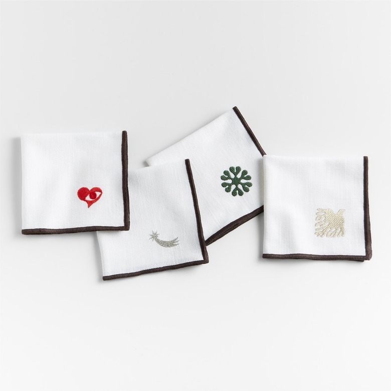 Four white napkins with black edges embroidered at the corner with one of Lucia Eames' favorite designs: her captivating Seeing with the Heart emblem in red