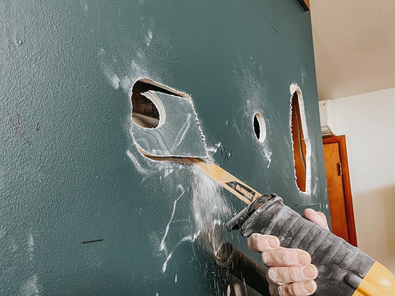 Cut exploratory holes through the drywall using a reciprocating saw.
