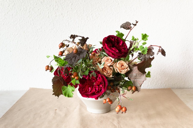 a diy floral centerpiece made of caramel roses and red flowers including ranunculus and zinnias