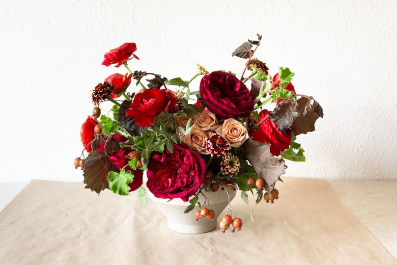 a diy floral centerpiece made of caramel roses and red flowers including ranunculus and zinnias