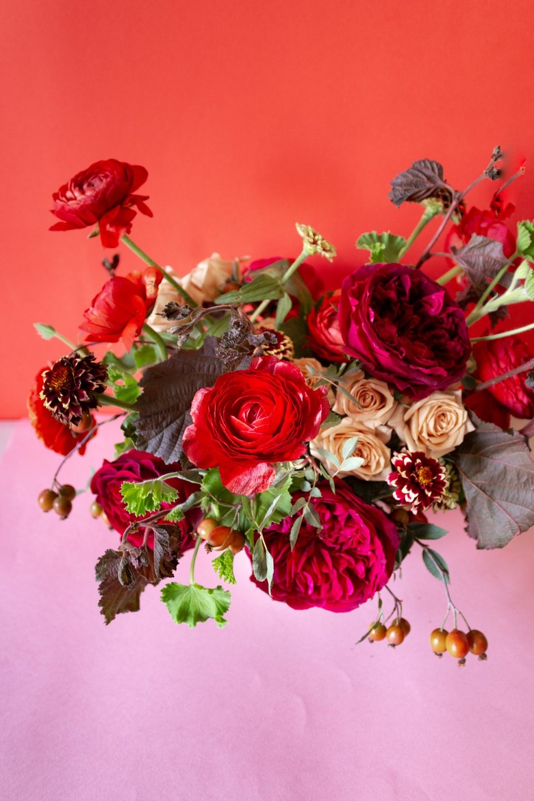 a diy floral centerpiece made of caramel roses and red flowers including ranunculus and zinnias