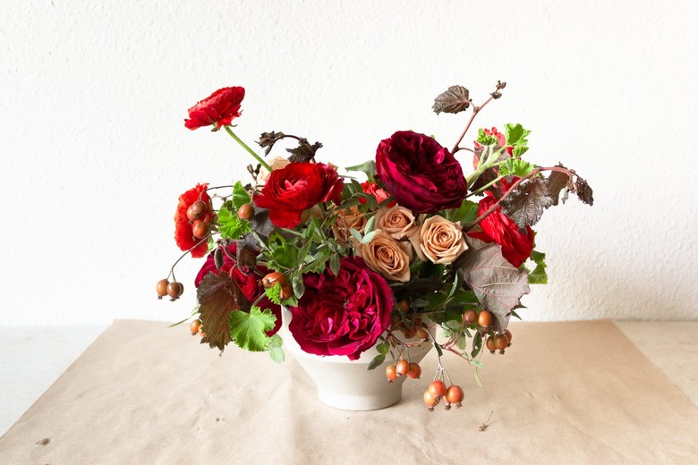 a diy floral centerpiece made of caramel roses and red flowers including ranunculus and zinnias