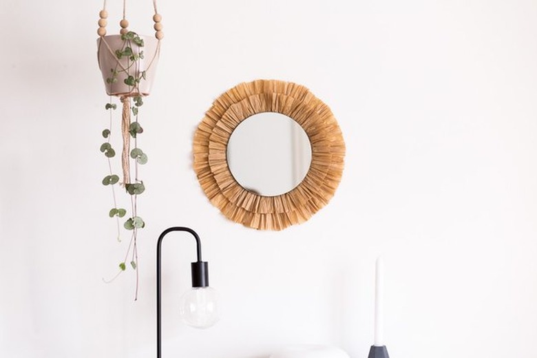 Raffia mirror on wall next to hanging plant.
