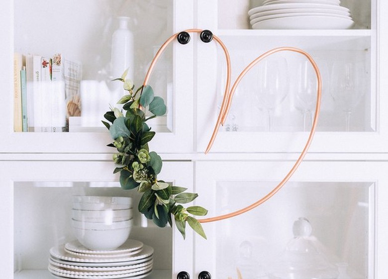Copper pipe heart wreath hanging on glass kitchen cabinet.