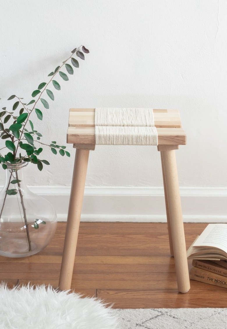 IKEA wood stool with rope details next to glass vase with greenery.