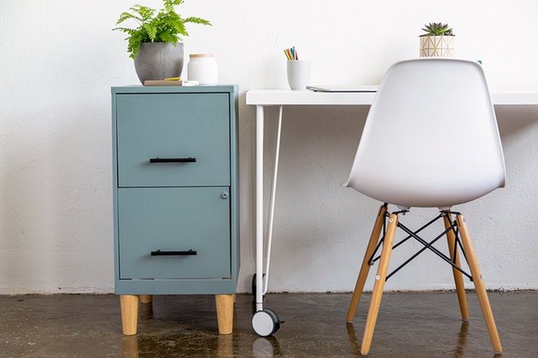 Blue painted filing cabinet next to white desk and modern chair.