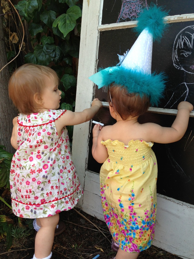 Two toddlers drawing on reclaimed door with chalkboard painted–glass panes in backyard