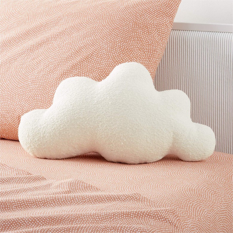 A cloud-shaped white pillow on a res pattern bedspread and pillow.