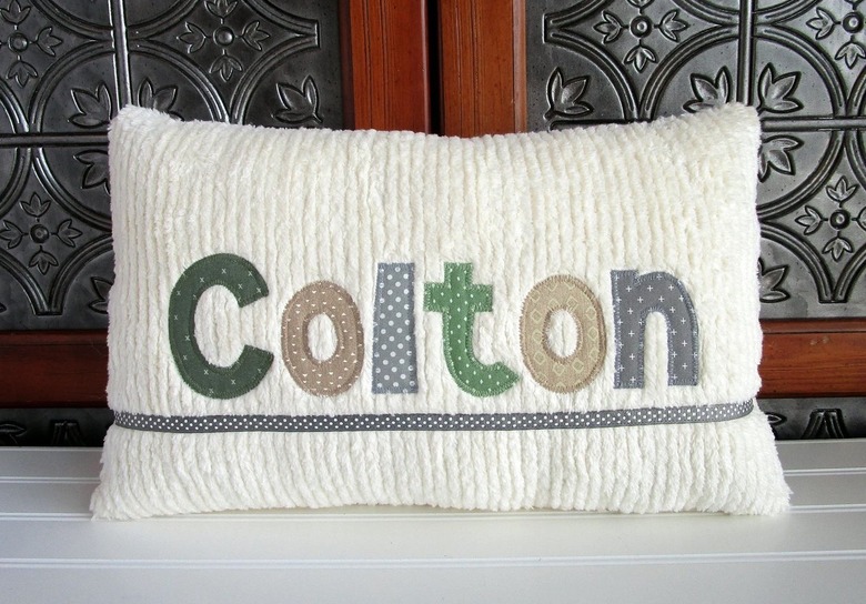 A white pillow with the name Colton in the center. Each letter has a different plain color or dotted pattern.