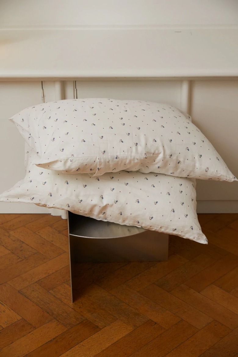 Stack of white pillows with floral design on a hardwood floor in front of a white wall