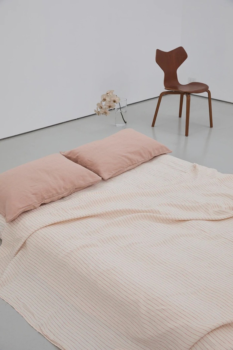 Clay pink sheets and blanket on a mattress on the floor. Behind the bedding is a white wall