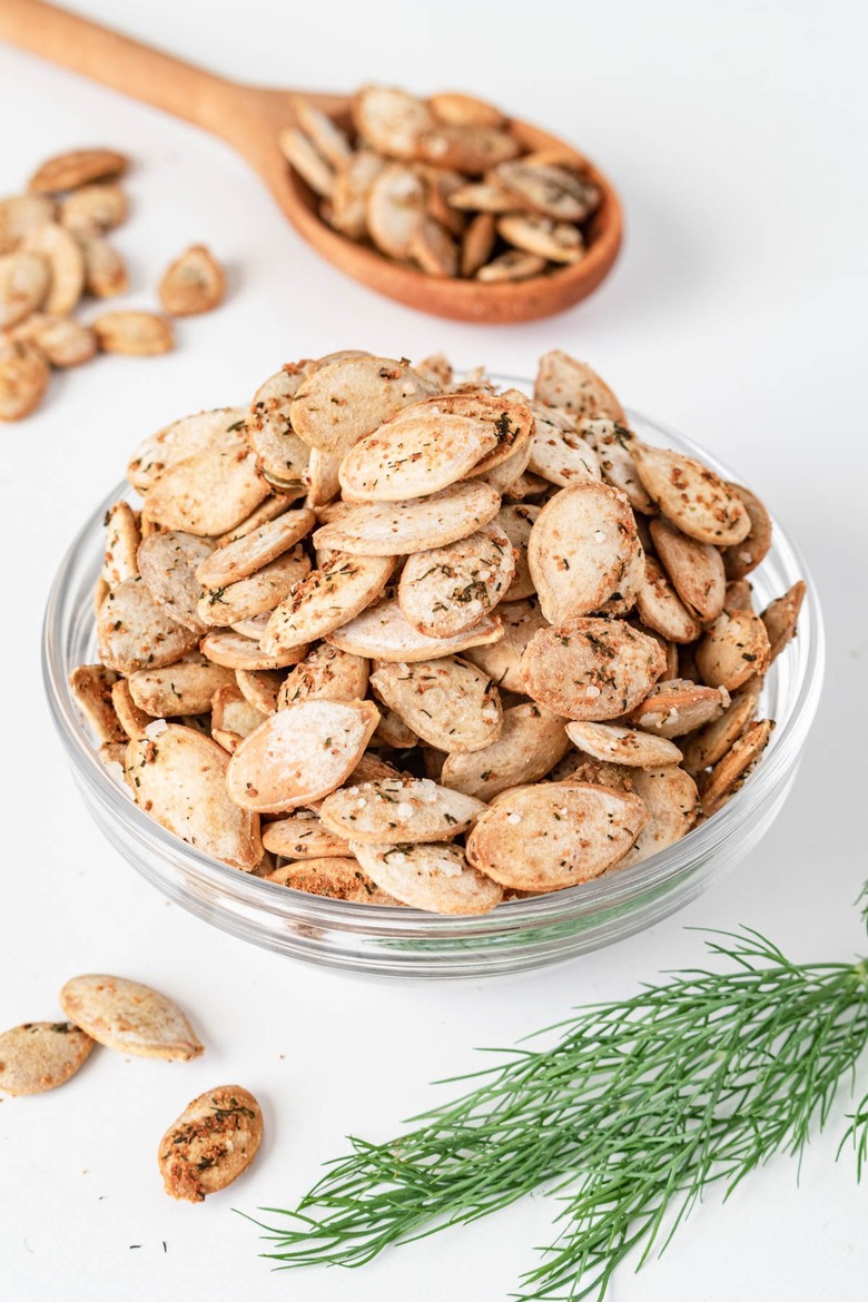 A small glass bowl filled with the dill pumpkin seeds on a white countertop.
