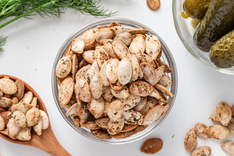 A small glass bowl filled with the roasted dill pumpkin seeds. You can also see a wood spoon holding the pumpkin seeds