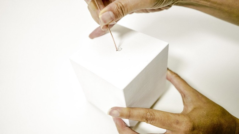 inserting a wire plant holder into a hole drilled into a wooden block