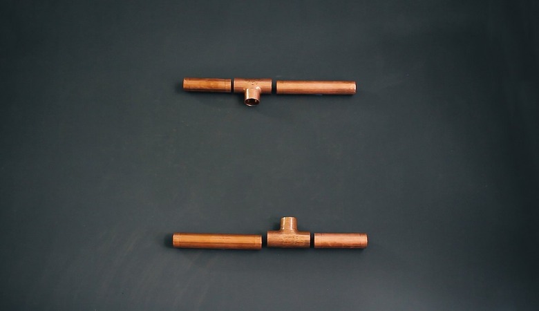 pieces of copper pipe that will become opposite sides of a candelabra base laid out on a table