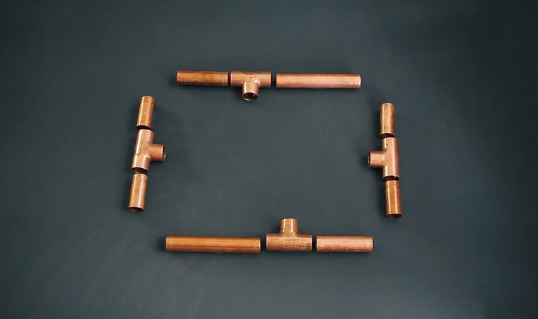 pieces of copper pipe that will become the four sides of a candelabra base laid out on a table