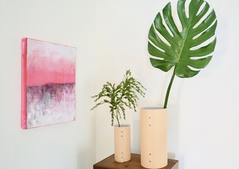 Leather vases holding monstera leaf and greenery