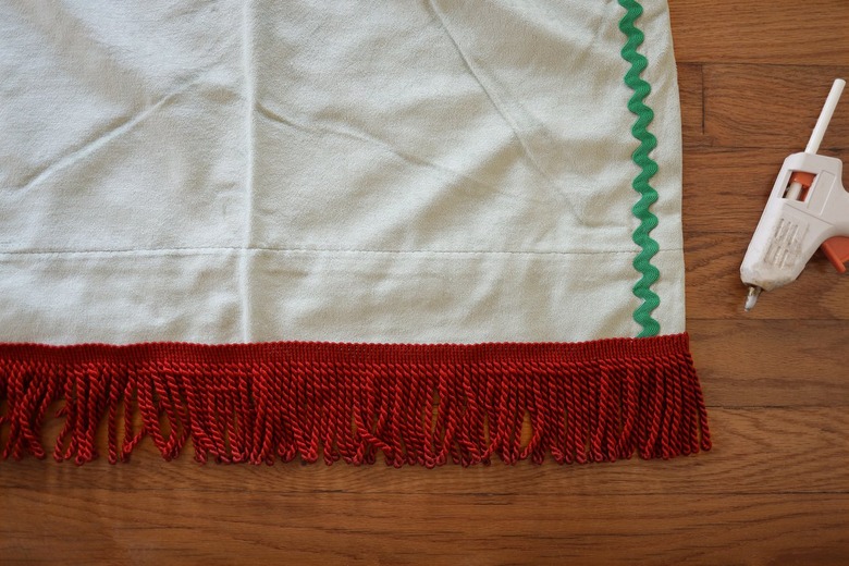 Hot gluing brick red bullion fringe to bottom of velvet curtain