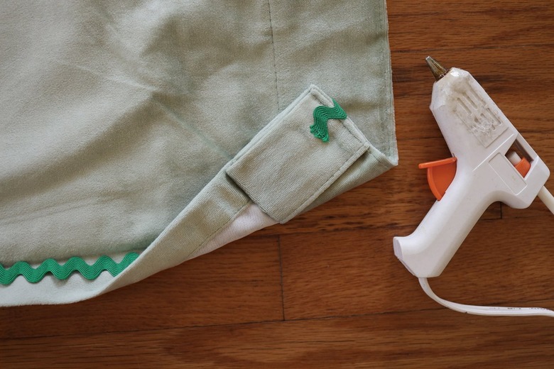 Hot gluing emerald green rick rack trim along edge of velvet curtain