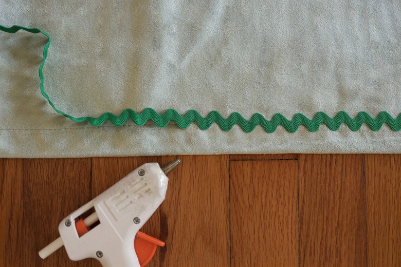 Hot gluing emerald green rick rack trim along edge of velvet curtain