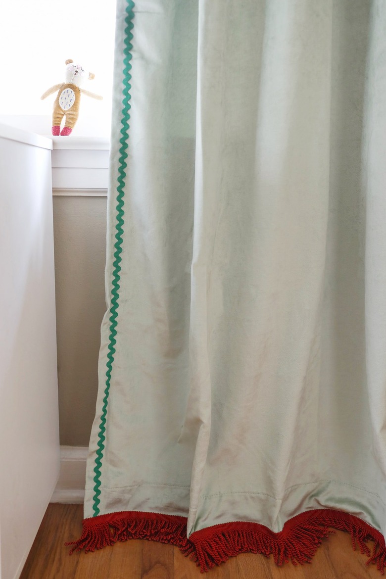 Sage green velvet curtains with brick red fringe trim on the bottom and emerald green rick rack trim on the side
