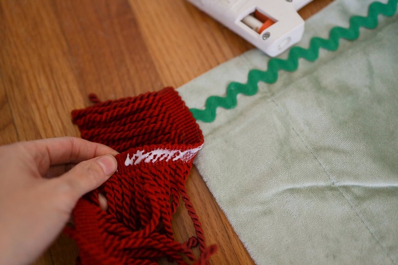 Hot gluing brick red bullion fringe to bottom of velvet curtain