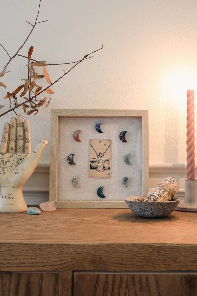 Shadow box with tarot card and moon-shaped crystals on table with palmistry hand