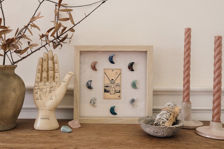 Shadow box with tarot card and moon-shaped crystals on table with palmistry hand