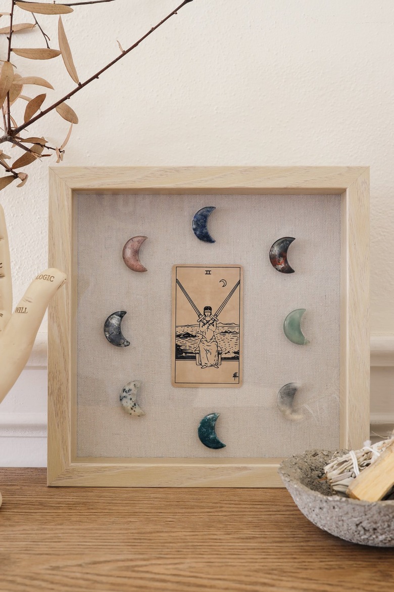 Shadow box with tarot card and moon-shaped crystals on table with palmistry hand