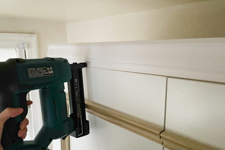 Brad nailing crown molding to scrap wood on top of IKEA PAX wardrobe