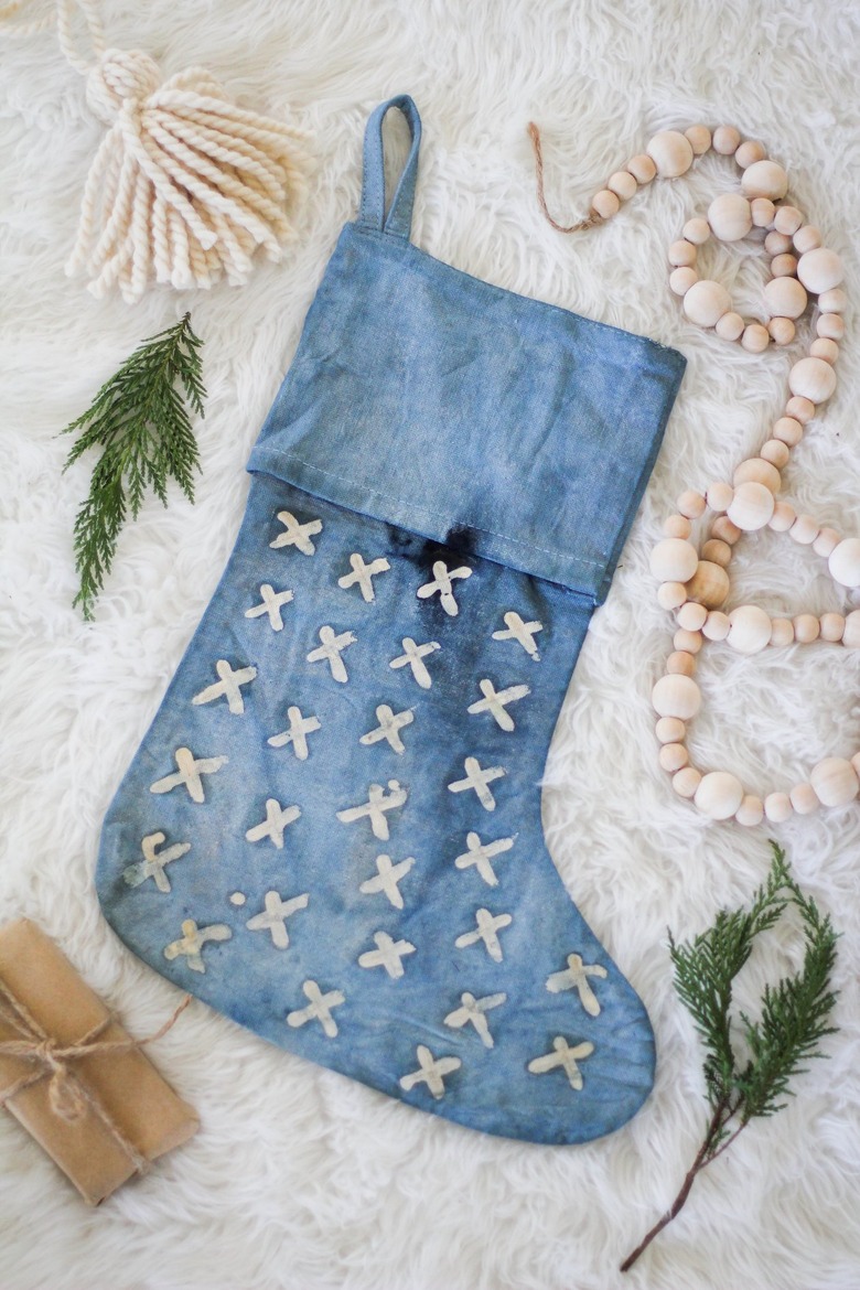 Indigo stocking with stitched white x's surrounded by decorative fir and decorations