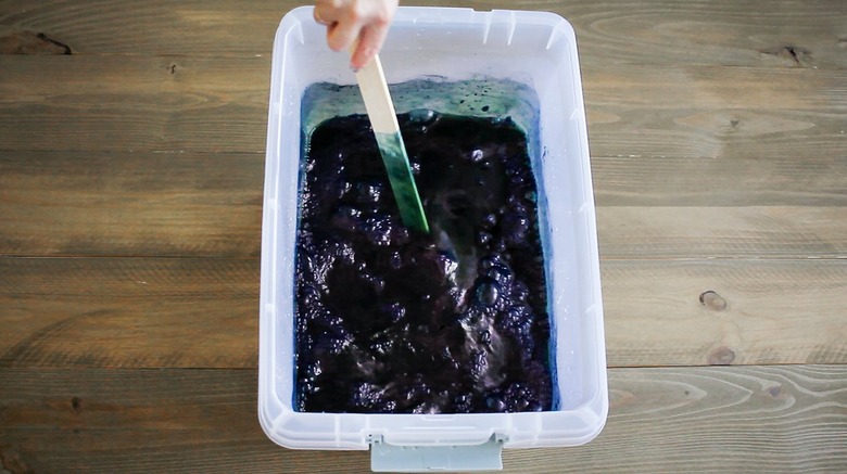 Hand stirring indigo dye in bucket with paint stick