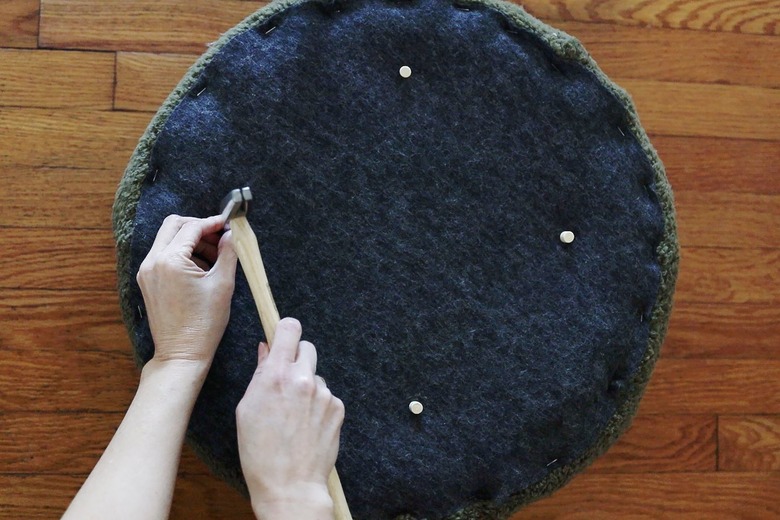 Hammering four wooden thumb tacks 3 inches in from edge to prevent lid from slipping off stool