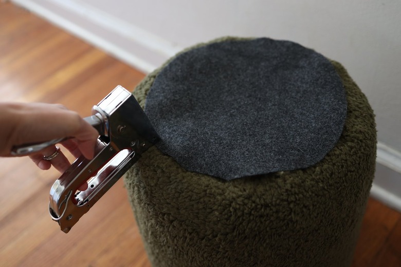 Stapling gray felt fabric circle to bottom of upholstered bucket