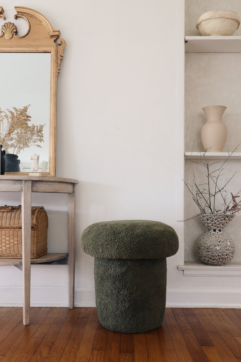Green sherpa mushroom stool next to table with gold mirror and shelf with vases