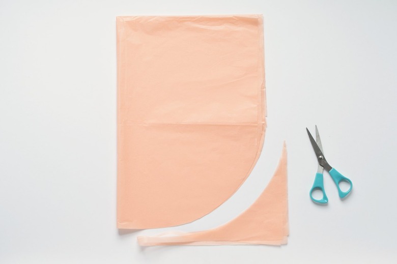 Cut curved tissue paper with turquoise-handled scissors against a white background