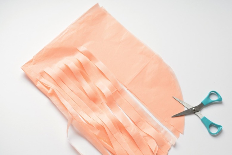 Partially cut paper fringe with turquoise-handled scissors against a white background