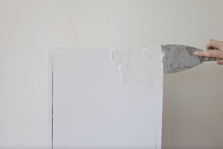 Applying joint compound with putty knife to plinth