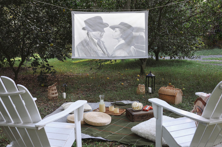 DIY portable projector screen hanging outside between two trees with chairs