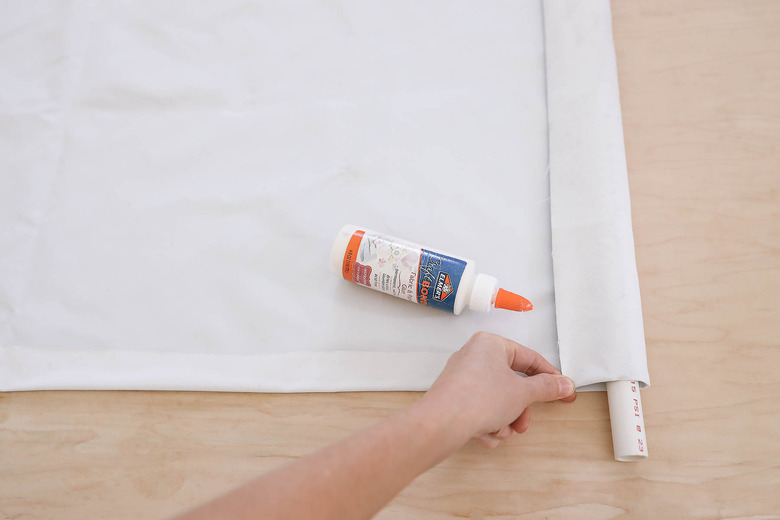 Folding and gluing raw edge around a PVC pipe placed along bottom of blackout fabric
