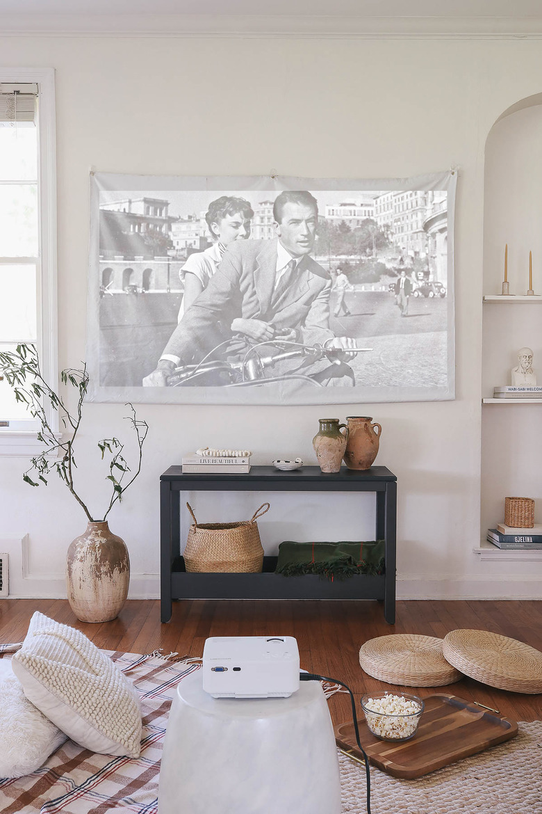 DIY portable projector screen hanging on wall of living room with blankets and pillows on floor and bowl of popcorn on tray